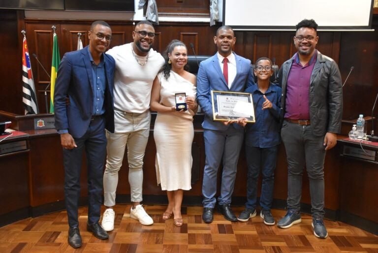 Representantes da UNEI participam de uma cerimônia de homenagem em uma Câmara Municipal. O grupo posa para uma fotografia ao lado de um homenageado que segura uma placa de reconhecimento, simbolizando a valorização da atuação da organização e de suas lideranças na promoção da igualdade racial e da cultura negra.